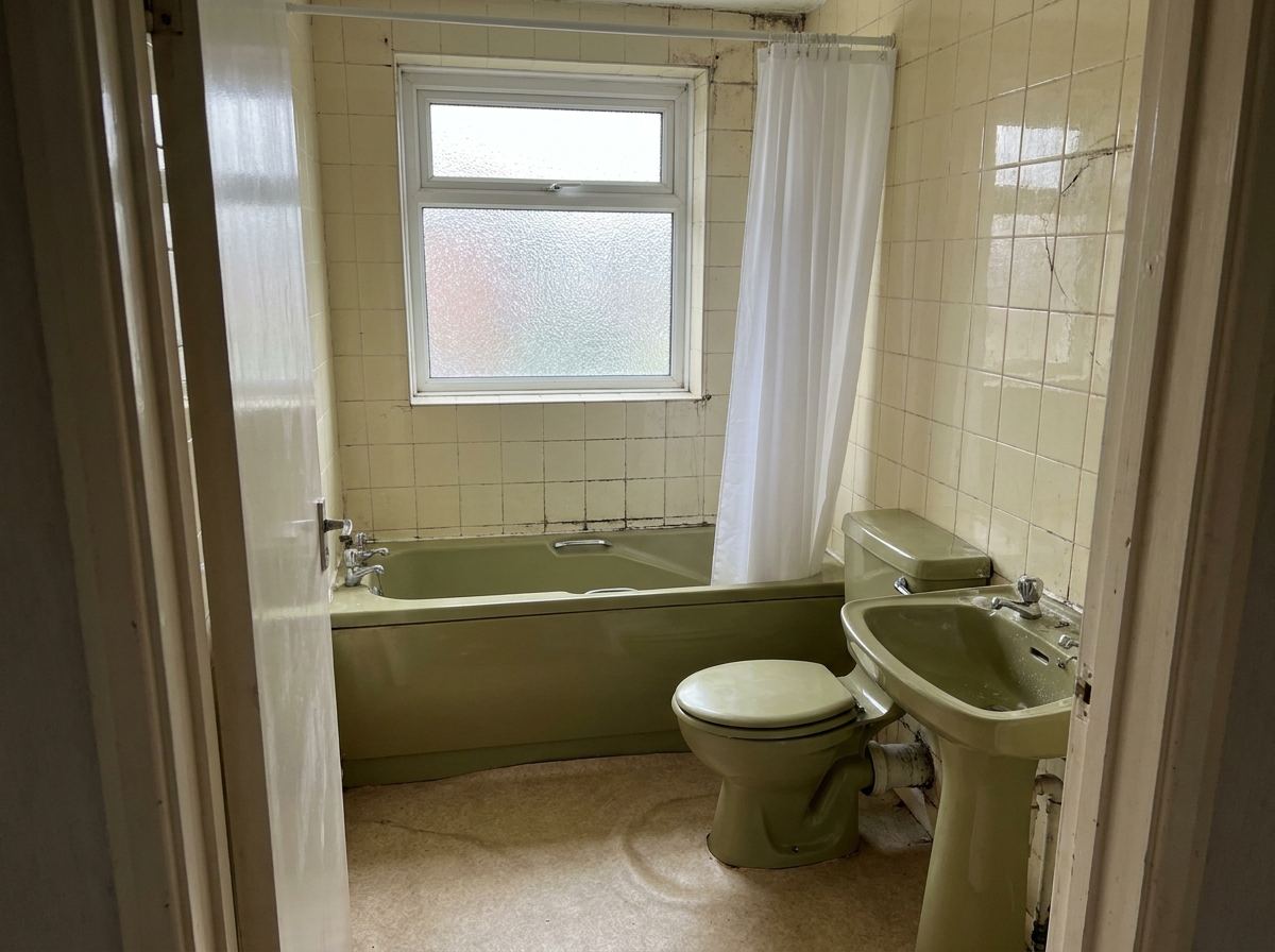 A tired family bathroom with an old green suite, cracked cream tiles and worn flooring